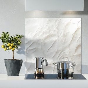 Puede incluir: Una escena de cocina con un pequeño limonero en maceta con frutos amarillos, una cafetera exprés de acero inoxidable y una olla cubierta de acero inoxidable. Una placa para salpicaduras blanca texturizada está detrás de los electrodomésticos.