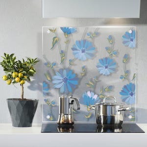 May include: A clear glass kitchen splashback featuring a blue floral pattern. A stainless steel saucepan and a coffee maker are on a black hob. A small potted lemon tree is on the left.