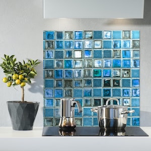 Puede incluir: Un protector de salpicaduras de cocina con un diseño de mosaico de azulejos azules y grises. Una cafetera y una olla con tapa están sobre una encimera de cocina negra.