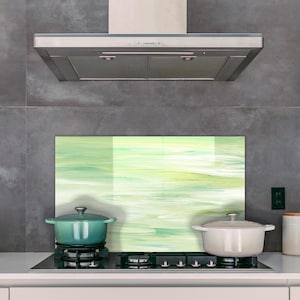 Könnte beinhalten: Eine Küchenszene mit einem Herd mit einem tealfarbenen Topf und einem weißen Topf. Eine dekorative Rückwand mit einem grün-weißen abstrakten Design befindet sich hinter den Töpfen. Eine weiße Teekanne und Kanister stehen auf der Theke.