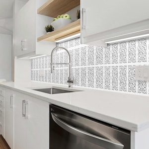 May include: A white kitchen with white cabinets, a stainless steel sink, and a white countertop. The backsplash is a black and white patterned tile. There is a stainless steel dishwasher under the countertop.