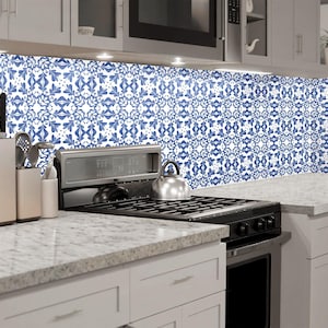 May include: A white kitchen with blue and white patterned tile backsplash, a stainless steel hob, and white cabinets.