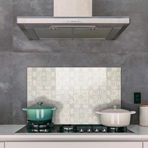 May include: A modern kitchen scene featuring a gas cooktop with two pots, one teal and one white. A decorative backsplash with a floral pattern is behind the cooktop. A stainless steel range hood is above the cooktop.