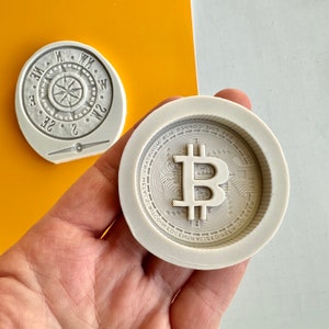 May include: A white silicone mold for making a chocolate replica of a Bitcoin coin. The mold features the Bitcoin logo and the text "999 FINE COPPER YATATVIOM MELTVZ BISCOIN EDECENTRALIZED BEER TO BEER".