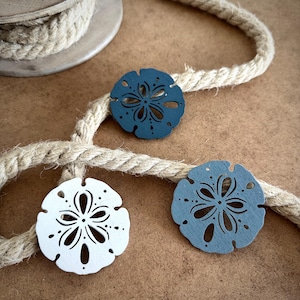 May include: Three sand dollar ornaments, one white, one dark blue and one light blue, with a rope behind them.