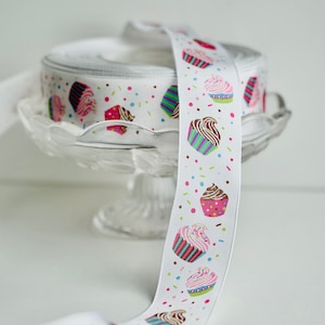 May include: White satin ribbon with a repeating pattern of colourful cupcakes and sprinkles.