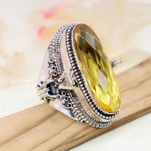 May include: A large, ornate silver ring featuring a faceted, elongated yellow gemstone. The ring has intricate detailing around the stone and along the band, with a vintage or antique aesthetic. The gemstone is the focal point, catching the light.