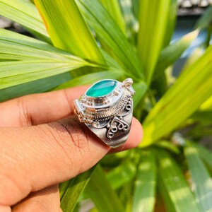 May include: A silver ring with an oval, bright green gemstone. The ring has intricate, ornate detailing around the stone and on the band. The gemstone is the focal point, set in a detailed silver setting. The ring is a piece of jewelry.