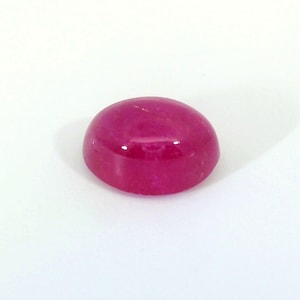 Op de afbeelding: Een gepolijste, ovaalvormige robijn edelsteen. De edelsteen heeft een diepe, levendige roodroze kleur met een glad, glanzend oppervlak. De edelsteen is geplaatst tegen een effen witte achtergrond.