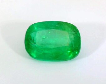 Puede incluir: Una gema de esmeralda verde vibrante con un corte de cojín. La esmeralda es lisa y pulida, con una ligera forma ovalada.