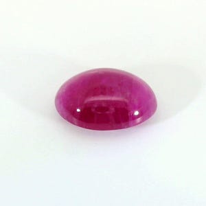 Puede incluir: Una gema ovalada de color rosa vibrante con una superficie lisa y pulida.