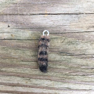 May include: A small, brown and black striped felt raccoon charm with a silver jump ring.