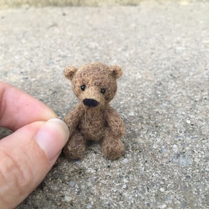 May include: A miniature brown teddy bear with a black nose and small, round ears. The bear is made of a textured material and is sitting upright. The bear is a handmade item.