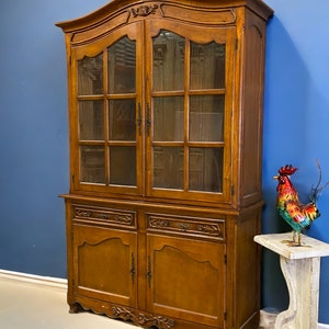 May include: A large, antique, wooden cabinet with glass doors and drawers. The cabinet has a curved top and intricate carvings. The cabinet is a rich brown color and has a distressed finish.