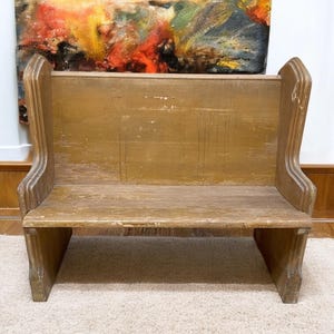 May include: A vintage wooden bench with a distressed, aged appearance. The bench features a backrest and armrests, painted in a muted, yellowish-brown color. The bench is designed with a simple, functional aesthetic, suitable for seating.