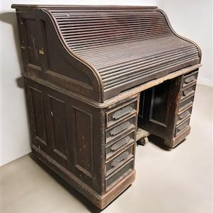 May include: An antique roll-top desk made of dark wood. The desk features a slatted roll-top cover, multiple drawers, and a sturdy, aged appearance. The desk is a classic piece of furniture.