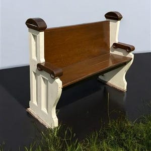 May include: A wooden church pew with a white painted base and a brown wooden seat and back. The pew has a simple design with a curved top and armrests.