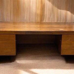 May include: A wooden desk with three drawers on each side. The desk has a dark brown finish and a simple design.