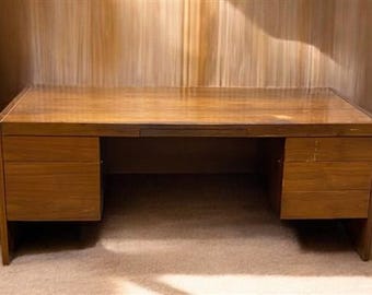 May include: A rectangular wooden desk with a polished brown finish. The desk features a wide flat top surface and two pedestals, one on each side. The left pedestal has one large drawer, while the right pedestal contains three stacked drawers.