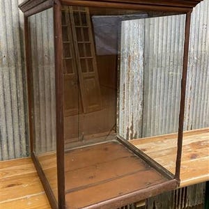 May include: A vintage wooden display case with glass sides and a wooden base. The case is empty and has a simple design.