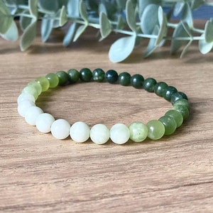 May include: A green and white jade gemstone bracelet with round beads. The beads are graduated in size, with the larger beads being green and the smaller beads being white.