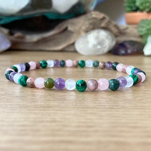 May include: A multi-colored beaded bracelet with pink, green, and purple beads. The bracelet is made of natural stones and is a popular choice for those who believe in the power of crystals.