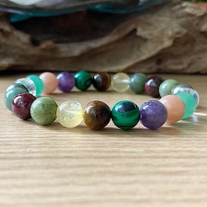 May include: A bracelet made of various colored gemstone beads, including green, brown, yellow, pink, purple, and red. The bracelet is made of round beads and is strung on a clear elastic cord.