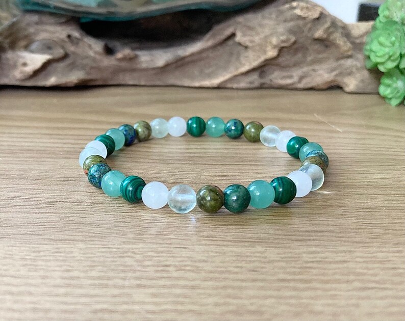May include: A green and white beaded bracelet with various shades of green and white beads. The bracelet is made of natural stones.