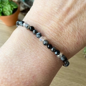 May include: A bracelet made of black, white, and gray beads. The bracelet is made of natural stones and is worn on a person's wrist.