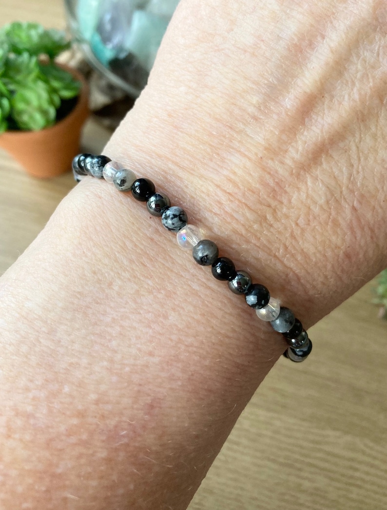 May include: A bracelet made of black, white, and gray beads. The bracelet is made of natural stones and is worn on a person's wrist.