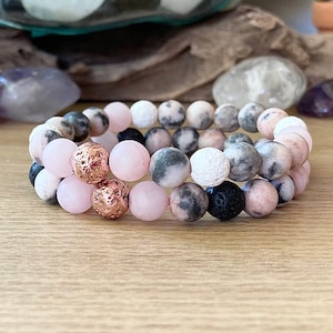 May include: Two stacked bracelets with pink, white, black and grey beads. The bracelets have copper accents.