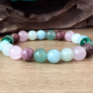 May include: A multi-colored beaded bracelet with pink, green, and blue beads. The bracelet is made of natural stones and is a popular choice for those who enjoy wearing jewelry with a spiritual or healing meaning.