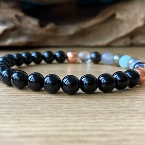 May include: A black beaded bracelet with a variety of other colored beads, including copper, clear, and green.