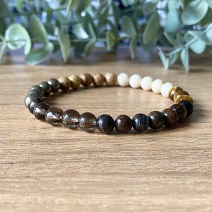 Peut inclure: Un bracelet en perles avec des perles brunes, noires, blanches et dorées.