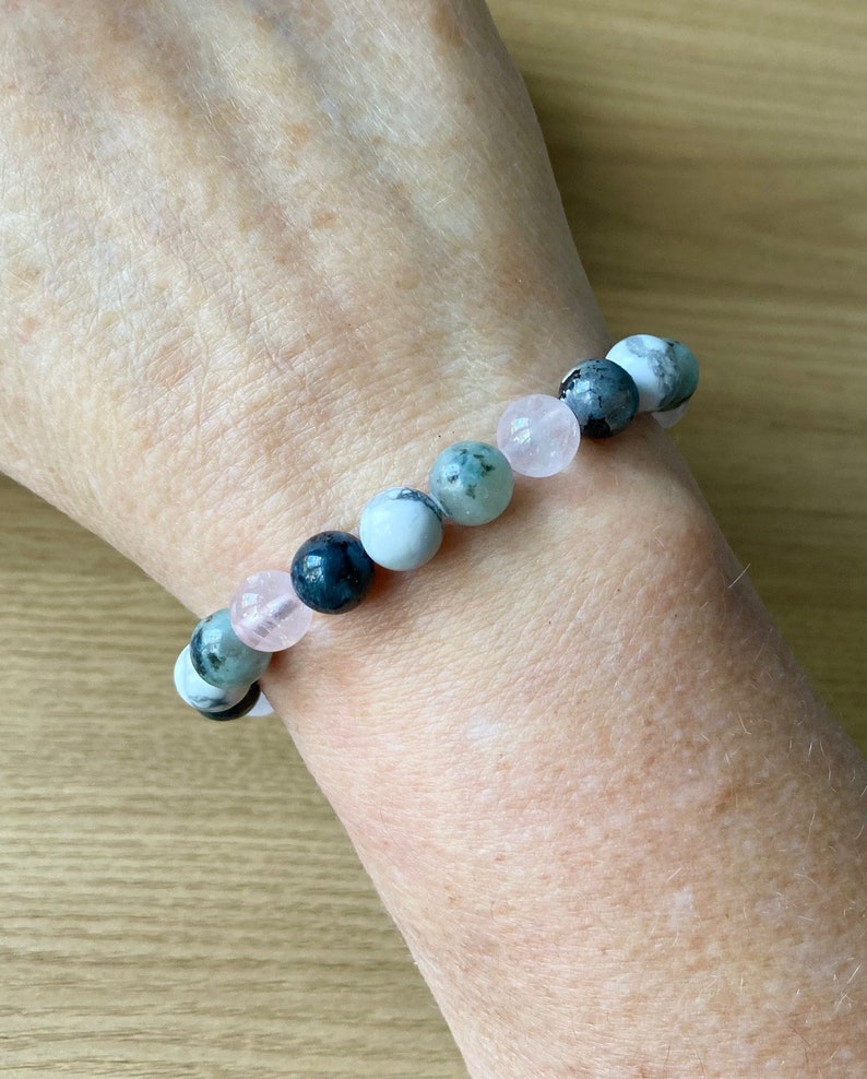 Puede incluir: Un brazalete hecho de cuentas de piedras preciosas verdes, blancas y rosas. El brazalete est&aacute; en la mu&ntilde;eca de una persona.
