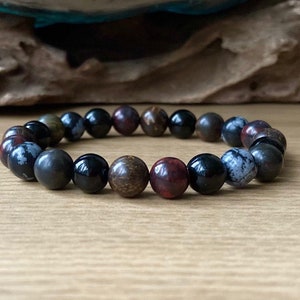 May include: A beaded bracelet with black, brown, and red stones. The bracelet is made of natural stones and is designed to be worn on the wrist.