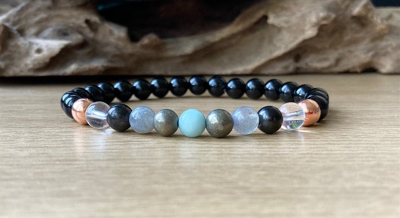 May include: A black beaded bracelet with a variety of gemstone beads, including clear, grey, and green beads. The bracelet also features two copper beads.