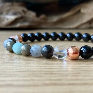 May include: A black beaded bracelet with a variety of gemstone beads, including clear quartz, black onyx, pyrite, and green aventurine.