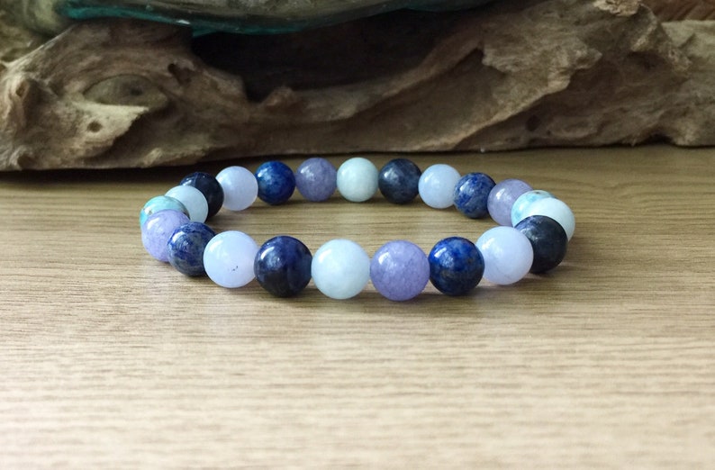May include: A bracelet made of blue, light blue, and purple gemstone beads. The bracelet is on a wooden surface.