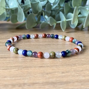 May include: A beaded bracelet featuring a repeating pattern of small, polished spherical stones in various colours including deep blue, translucent white, earthy green, reddish-brown, and light purple, strung together on a flexible cord.