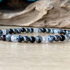 May include: A black, gray, and white beaded bracelet with a mix of round and oval beads.
