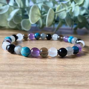 May include: A beaded bracelet with a variety of colors, including white, black, brown, blue, and purple. The bracelet is made of natural stones.