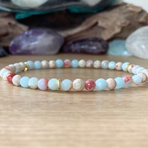 May include: A light blue and red gemstone bracelet with gold spacers. The bracelet is made of small, round beads.