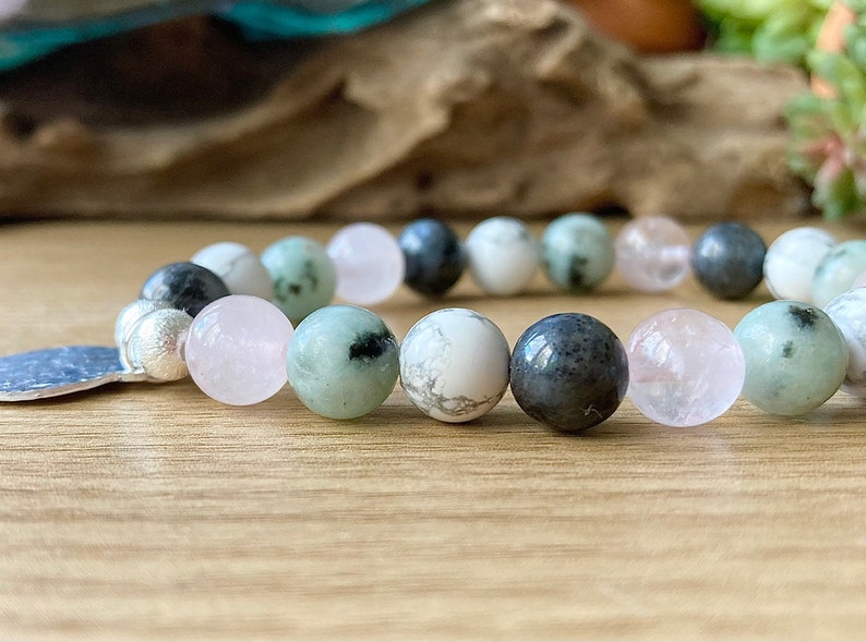 Puede incluir: Un brazalete hecho con cuentas verdes, blancas y rosas. El brazalete tiene un dije de plata.
