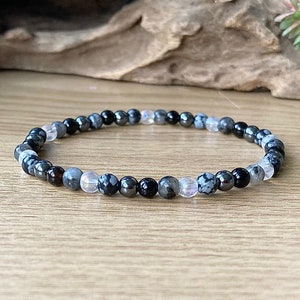 May include: A bracelet made of black, gray, and white beads. The beads are round and have a smooth finish. The bracelet is on a wooden surface.