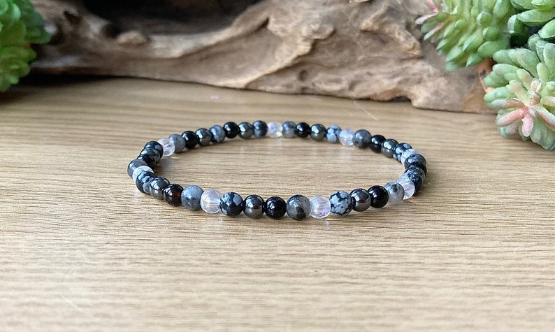 May include: A bracelet made of black, gray, and white beads. The beads are round and have a smooth finish. The bracelet is on a wooden surface.