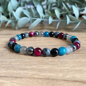May include: A beaded bracelet with a mix of grey, black, blue, and red beads.