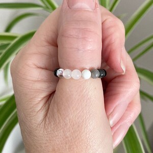 May include: A beaded bracelet with black, white and pink beads. The bracelet is worn on a person's thumb.