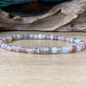 May include: A bracelet made of small, round, multi-coloured agate beads. The beads are a mix of white, grey, and pink with brown and white stripes.