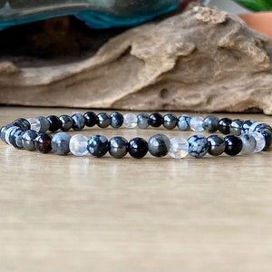 May include: A bracelet made of black, gray, and white beads. The beads are round and have a smooth finish. The bracelet is on a wooden surface.